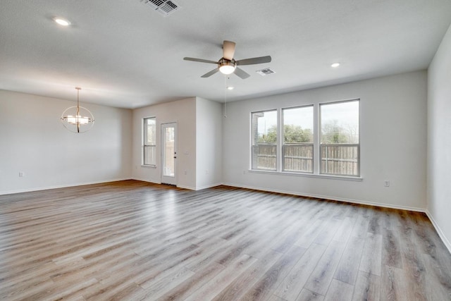spare room with plenty of natural light, visible vents, wood finished floors, and ceiling fan with notable chandelier