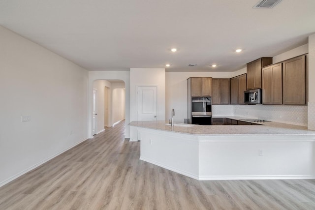 kitchen featuring arched walkways, stainless steel appliances, a sink, and light wood-style floors