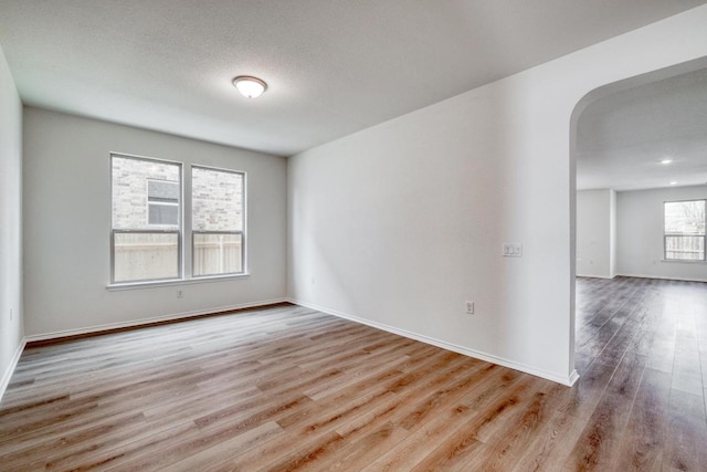 spare room with arched walkways, a textured ceiling, baseboards, and wood finished floors