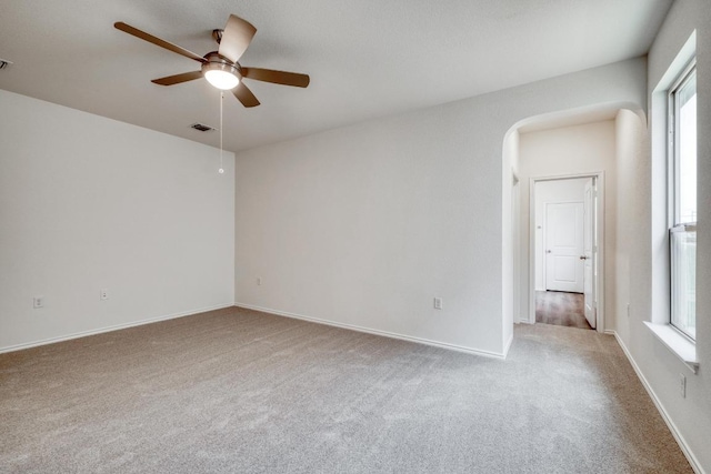 carpeted empty room featuring arched walkways, baseboards, visible vents, and a ceiling fan