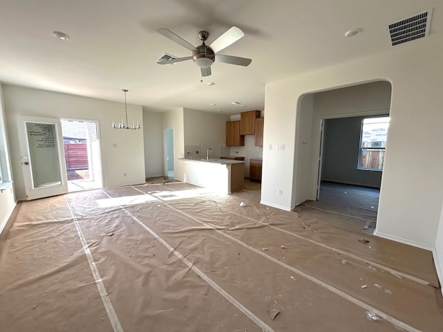 unfurnished living room featuring ceiling fan with notable chandelier and a wealth of natural light