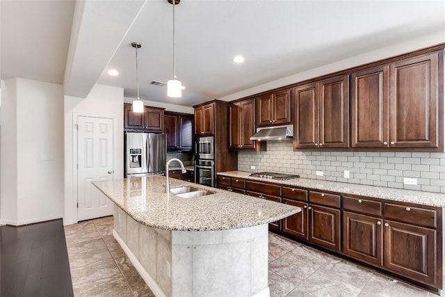 kitchen with appliances with stainless steel finishes, decorative light fixtures, sink, backsplash, and a kitchen island with sink