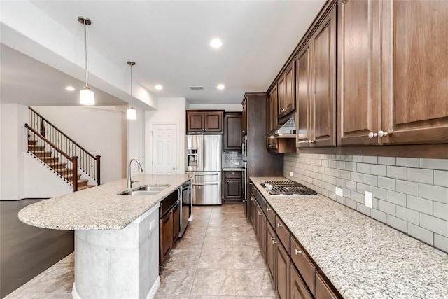 kitchen featuring backsplash, sink, hanging light fixtures, appliances with stainless steel finishes, and an island with sink