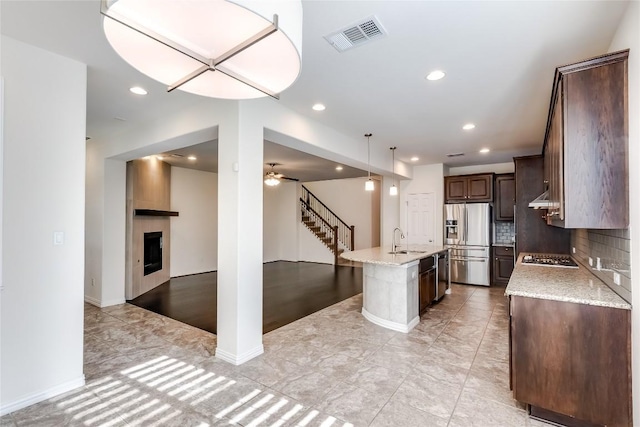 kitchen featuring appliances with stainless steel finishes, a fireplace, tasteful backsplash, sink, and a kitchen island with sink