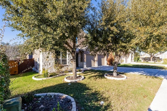 view of property hidden behind natural elements with fence, a front yard, a garage, stone siding, and driveway