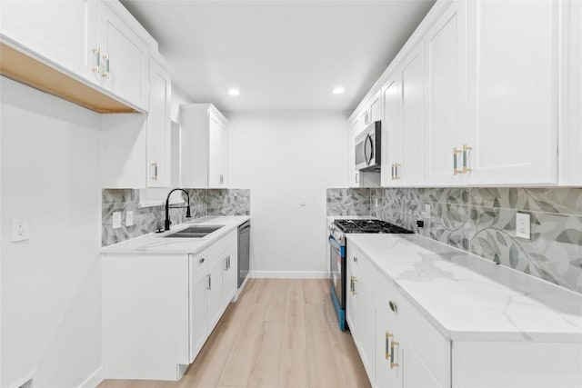 kitchen with light stone countertops, appliances with stainless steel finishes, sink, light hardwood / wood-style floors, and white cabinetry