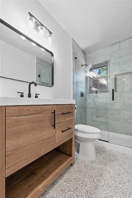 bathroom featuring tile patterned flooring, vanity, a shower with shower door, and toilet