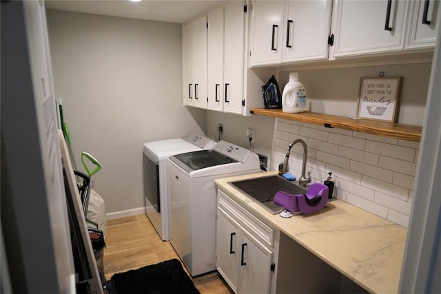 clothes washing area featuring washer and dryer, light hardwood / wood-style flooring, cabinets, and sink