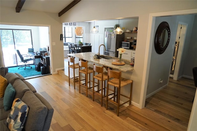 kitchen featuring appliances with stainless steel finishes, light stone counters, a breakfast bar, light hardwood / wood-style flooring, and hanging light fixtures