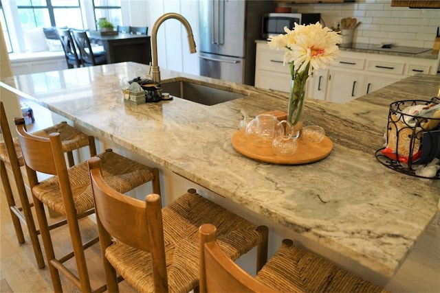 kitchen with white cabinetry, sink, light stone counters, backsplash, and a breakfast bar area