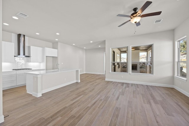 kitchen featuring white cabinetry, an island with sink, light hardwood / wood-style floors, and wall chimney range hood