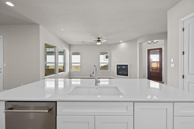 kitchen featuring ceiling fan, sink, light stone countertops, stainless steel dishwasher, and white cabinets