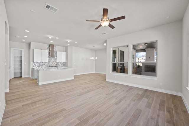 unfurnished living room with ceiling fan with notable chandelier and light hardwood / wood-style floors