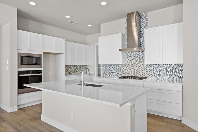 kitchen featuring wall chimney exhaust hood, sink, stainless steel appliances, and a kitchen island with sink