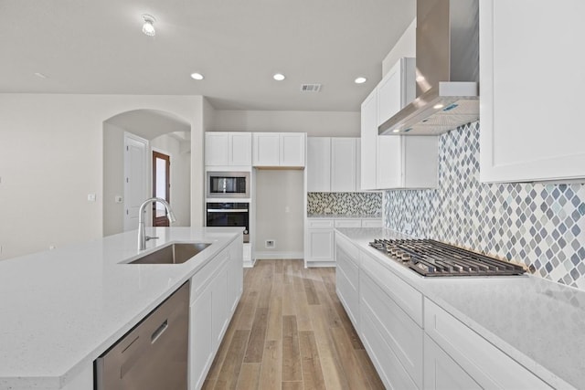 kitchen featuring wall chimney range hood, sink, light hardwood / wood-style floors, white cabinetry, and stainless steel appliances