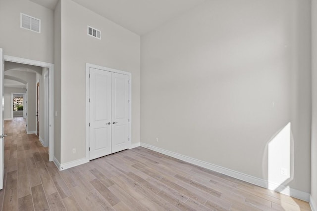 unfurnished bedroom with a high ceiling, light wood-type flooring, and a closet