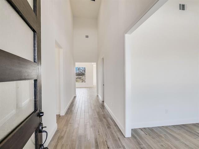 corridor featuring a towering ceiling and light hardwood / wood-style floors