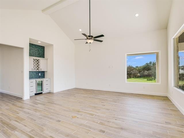 unfurnished living room featuring high vaulted ceiling, light hardwood / wood-style floors, bar, beam ceiling, and beverage cooler