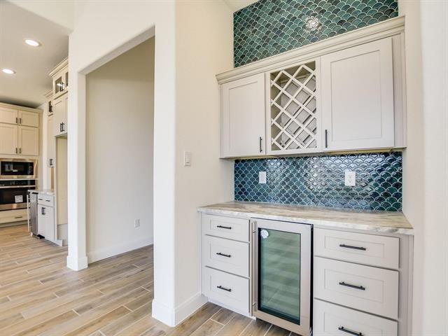 bar with white cabinetry, beverage cooler, wall oven, backsplash, and light hardwood / wood-style floors