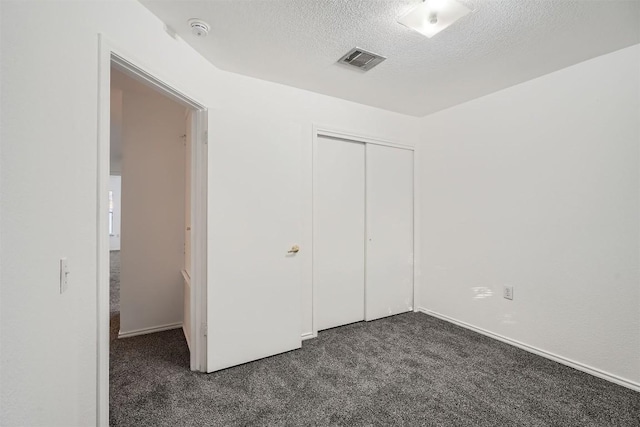 unfurnished bedroom with a textured ceiling, dark carpet, and a closet