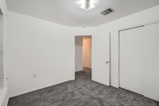 unfurnished bedroom with a textured ceiling, dark carpet, and a closet