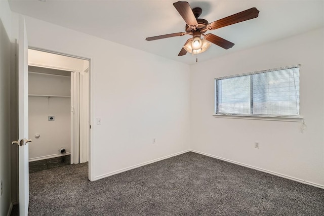 unfurnished bedroom with a closet, a spacious closet, dark carpet, and ceiling fan