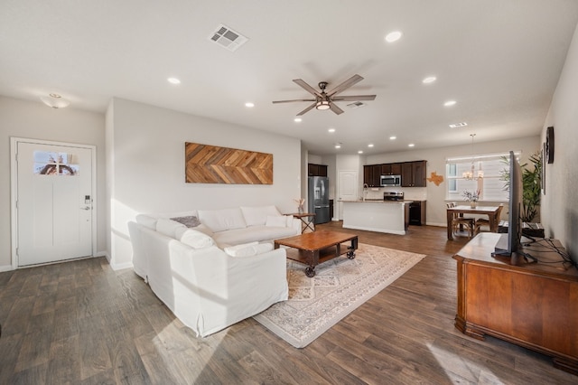 living room with ceiling fan with notable chandelier and dark hardwood / wood-style flooring