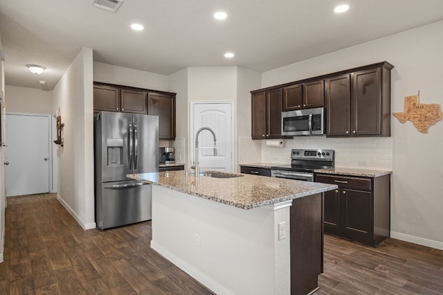 kitchen with sink, light stone counters, dark hardwood / wood-style floors, a center island with sink, and appliances with stainless steel finishes