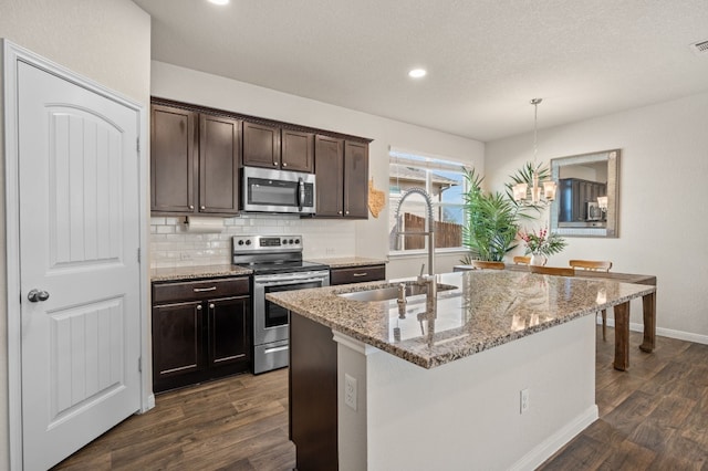 kitchen featuring light stone countertops, appliances with stainless steel finishes, sink, decorative light fixtures, and a center island with sink