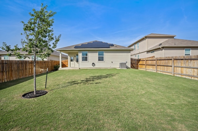 back of property with central AC, a yard, and solar panels