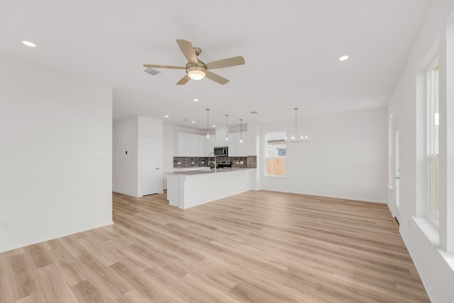 unfurnished living room with a sink, ceiling fan with notable chandelier, recessed lighting, light wood-type flooring, and visible vents