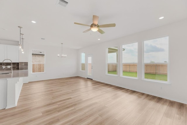 unfurnished living room featuring a sink, light wood-style flooring, ceiling fan with notable chandelier, recessed lighting, and visible vents