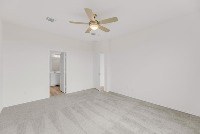 unfurnished bedroom featuring ceiling fan, light colored carpet, ensuite bath, and visible vents
