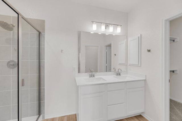 bathroom featuring a sink, a shower stall, double vanity, and wood finished floors