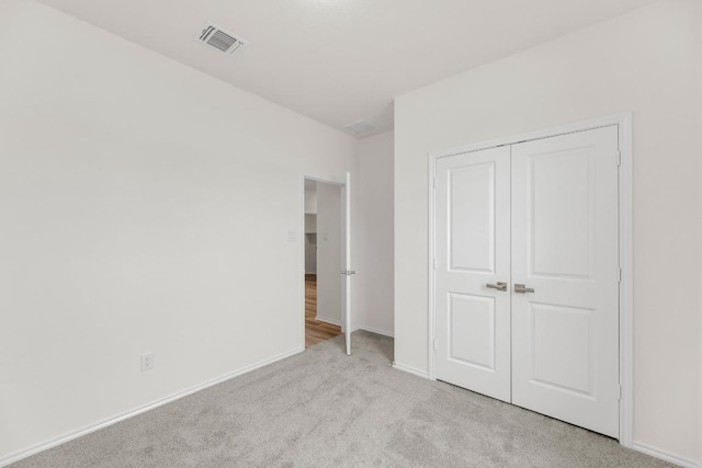 unfurnished bedroom with baseboards, visible vents, light carpet, and a closet