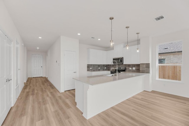 kitchen with decorative backsplash, appliances with stainless steel finishes, light wood-type flooring, light countertops, and a peninsula