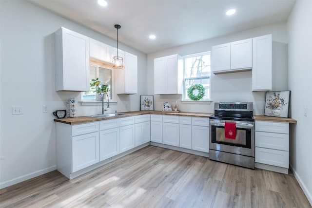 kitchen featuring sink, light hardwood / wood-style flooring, stainless steel stove, white cabinetry, and hanging light fixtures