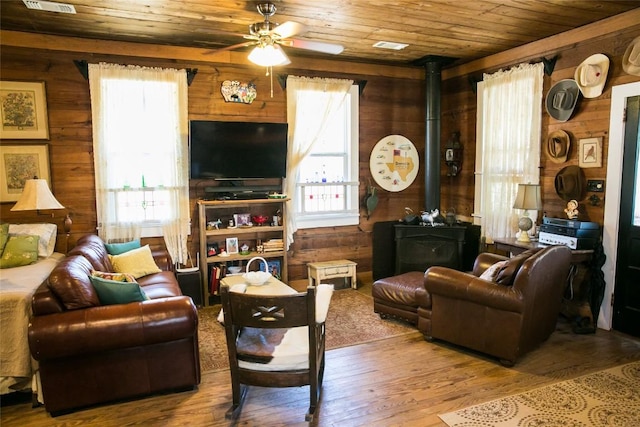 living room featuring hardwood / wood-style floors, wood walls, a wood stove, ceiling fan, and wood ceiling