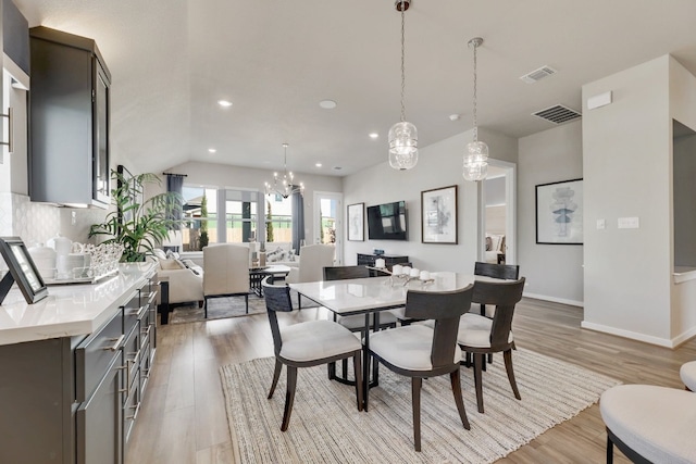 dining area with light wood-type flooring, an inviting chandelier, and vaulted ceiling