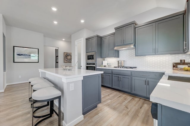 kitchen with a breakfast bar, a center island, light hardwood / wood-style flooring, decorative backsplash, and stainless steel appliances