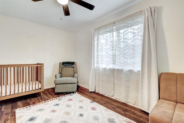 bedroom with ceiling fan, a crib, and dark wood-type flooring