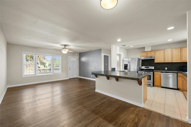 kitchen with a kitchen island, appliances with stainless steel finishes, tasteful backsplash, light hardwood / wood-style floors, and a kitchen bar