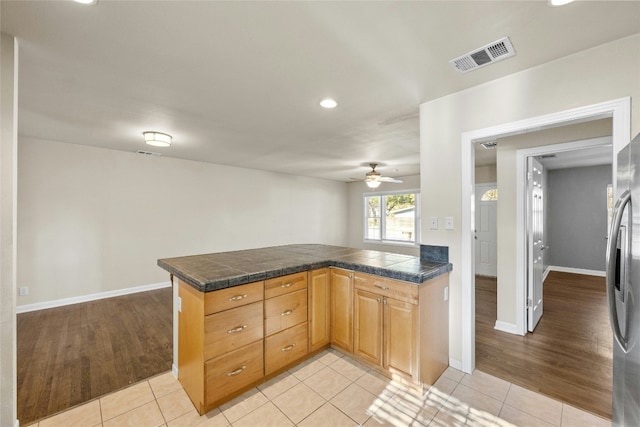 kitchen featuring ceiling fan, light tile patterned floors, kitchen peninsula, and stainless steel refrigerator