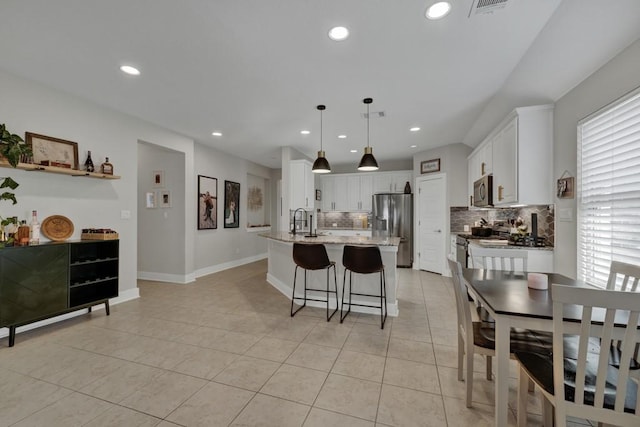 kitchen with appliances with stainless steel finishes, light tile patterned floors, decorative light fixtures, a center island with sink, and white cabinets