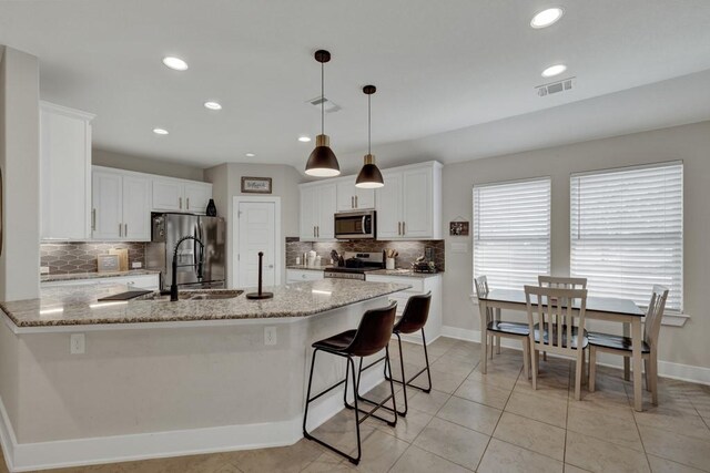 kitchen featuring light stone counters, white cabinets, decorative light fixtures, and appliances with stainless steel finishes