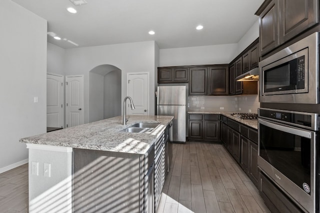 kitchen featuring dark brown cabinetry, sink, a kitchen island with sink, stainless steel appliances, and decorative backsplash