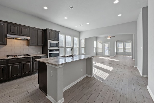 kitchen with backsplash, a center island with sink, sink, ceiling fan, and appliances with stainless steel finishes