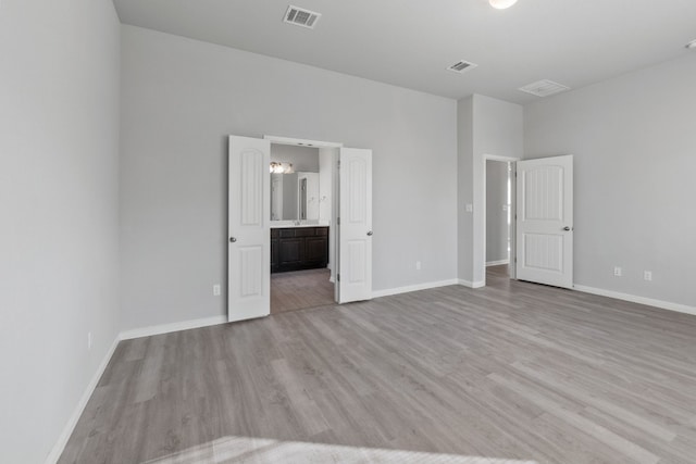 unfurnished bedroom with a high ceiling, light wood-type flooring, and ensuite bathroom