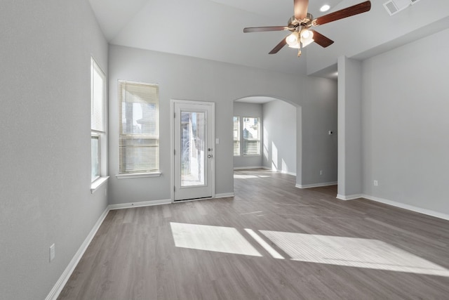 unfurnished living room featuring ceiling fan, a healthy amount of sunlight, vaulted ceiling, and light wood-type flooring