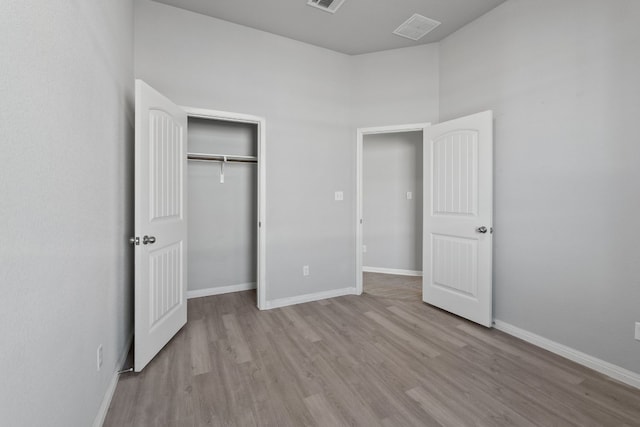 unfurnished bedroom featuring a closet, a towering ceiling, and light hardwood / wood-style flooring